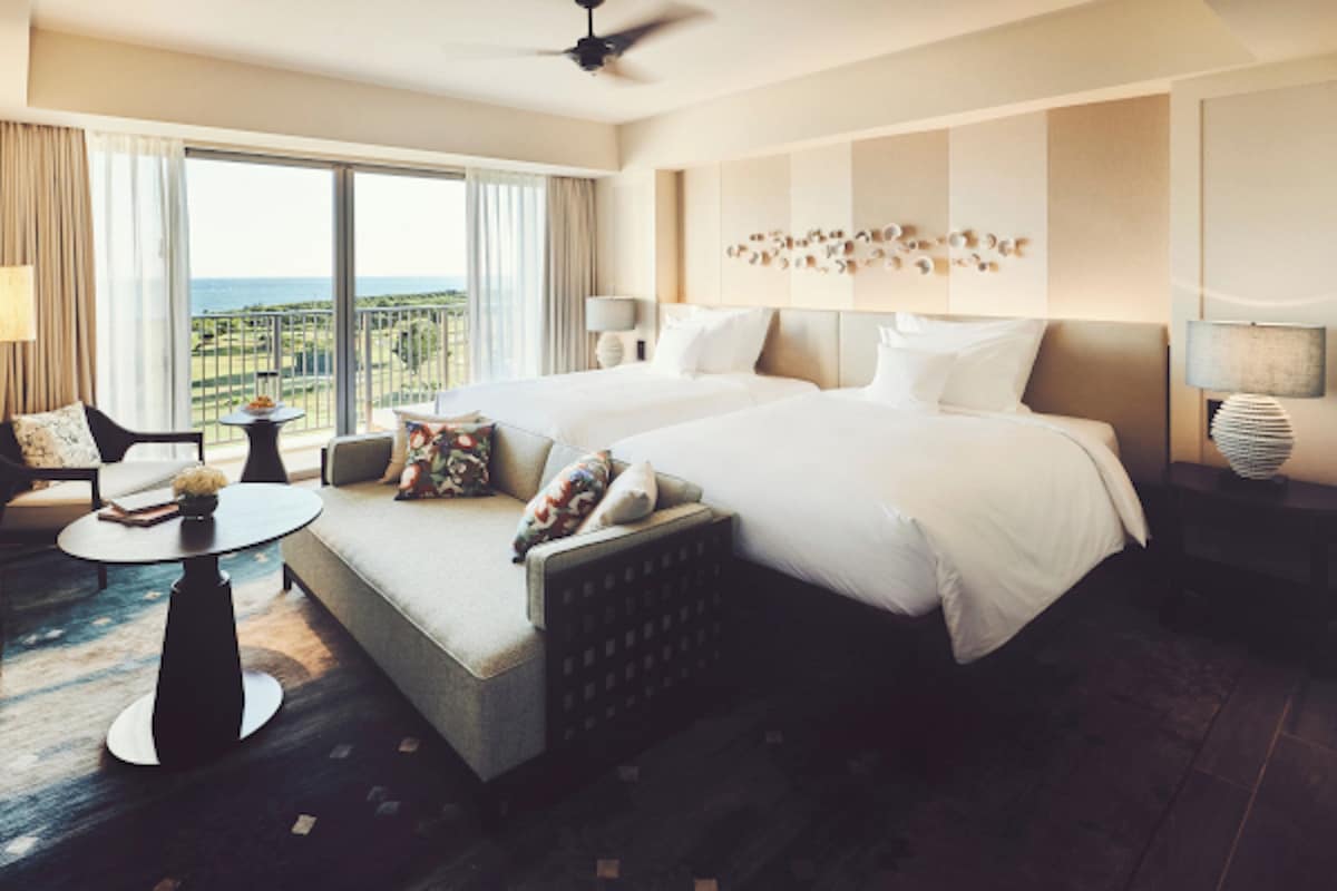 Amplia habitación de hotel con una cama grande, un sofá, una mesita y vistas al océano.