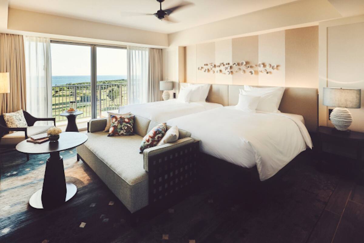 Une chambre d’hôtel spacieuse, dotée d’un grand lit, d’un canapé, d’une petite table et offrant une vue sur l’océan.
