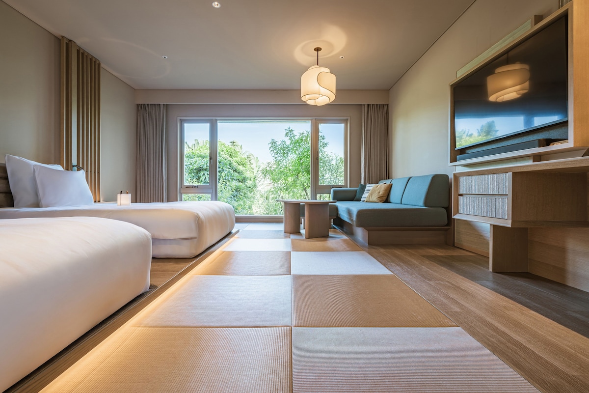 Habitación de hotel moderna con una cama grande, un sofá, un televisor y vistas a zonas verdes.