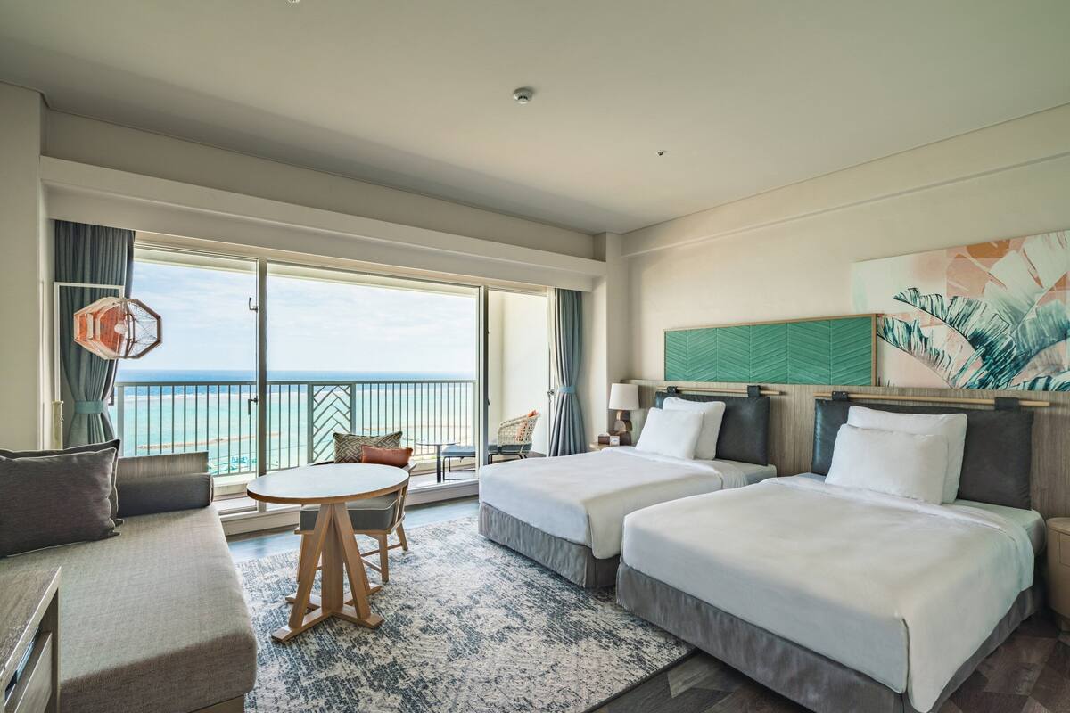Une chambre d’hôtel avec deux lits, un canapé, une table à manger et vue sur la mer.