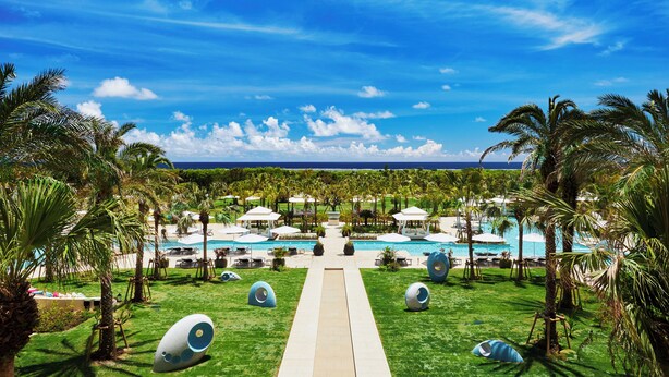 A resort with a central pool, lounge areas, and a view of the ocean.