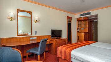 A hotel room with a desk, chair, television, wardrobe, and a bed.