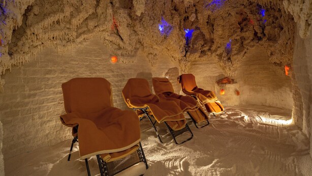 A spa with chairs arranged in a row, a stone wall, and a cave-like ceiling with blue lighting. - Ensana Thermal Sárvár (Sarvar)