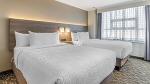 Quarto de hotel com duas camas, cabeceira de madeira, abajures e uma janela grande com cortinas.