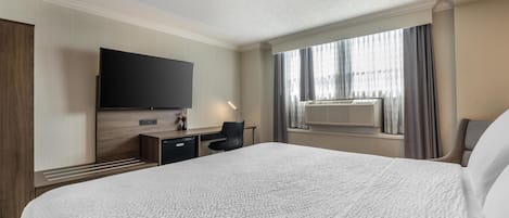 Habitación de hotel con una cama grande, un televisor de pantalla plana montado en la pared, un escritorio con silla y una ventana con cortinas.