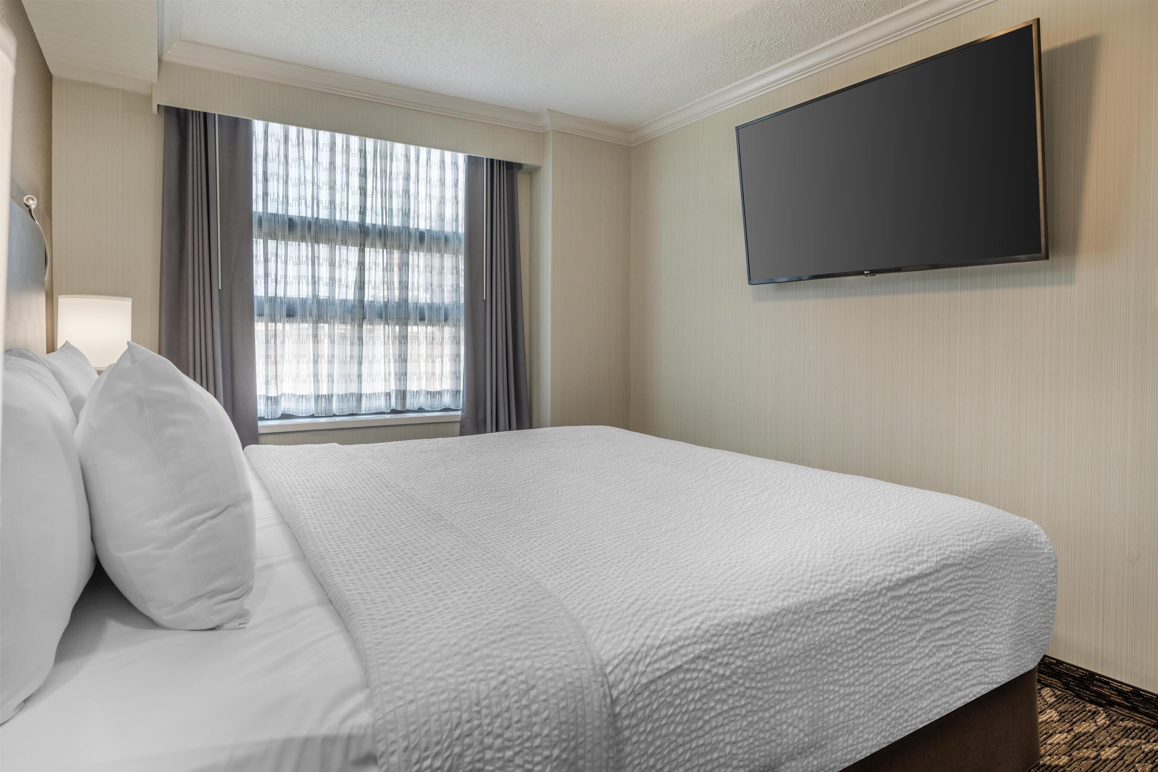 Une chambre d’hôtel avec un grand lit, un téléviseur à écran plat fixé au mur et une fenêtre avec des rideaux.