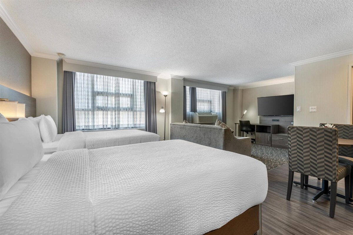 A hotel room with two beds, a desk, a chair, a television, and a large window with curtains.