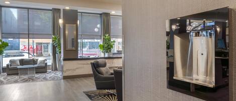 Eine moderne Hotellobby mit einer Couch, Sesseln und einem großen Fenster mit Blick auf die Straße.