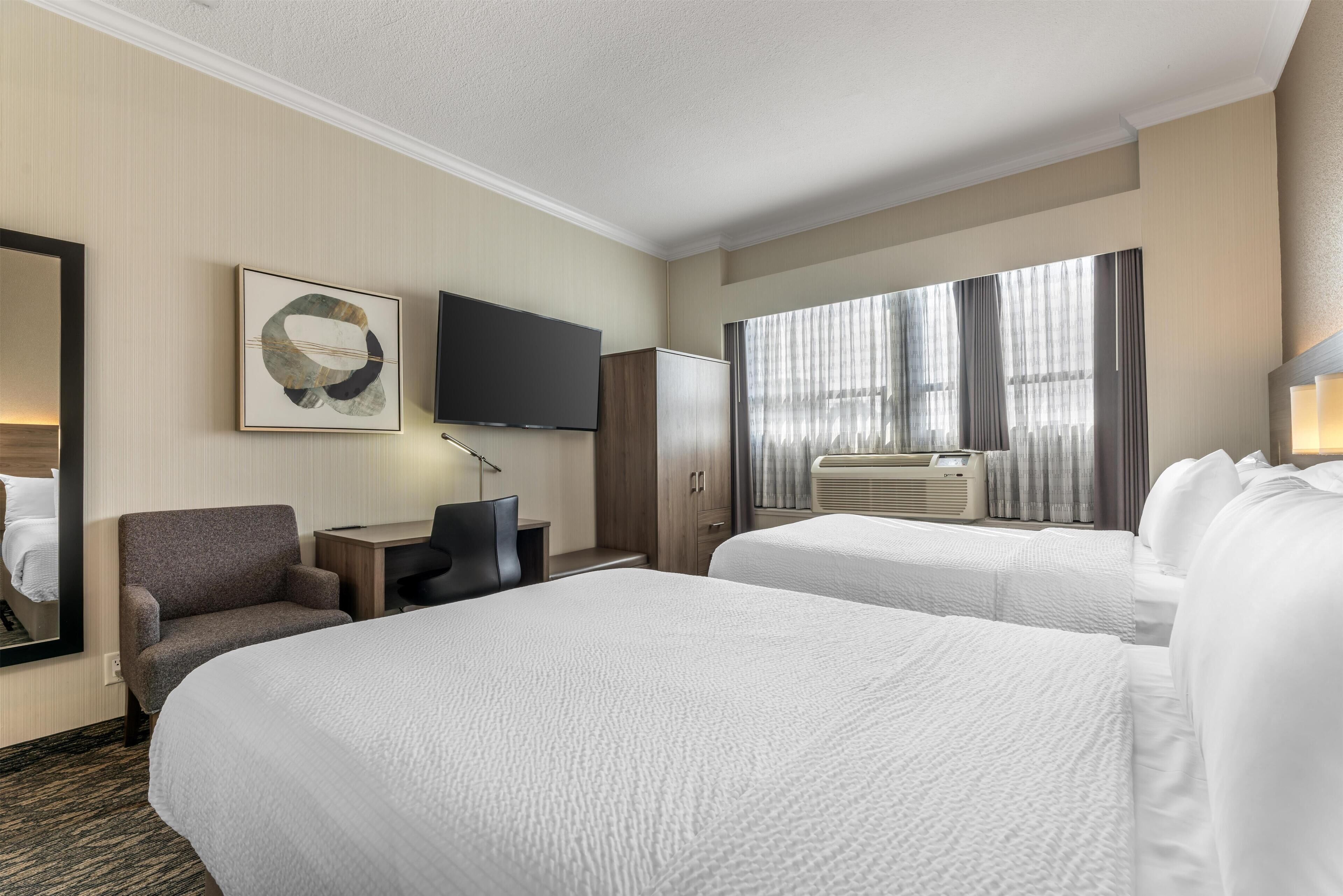 A hotel room with two beds, a desk, a chair, a TV, and a large window with curtains.