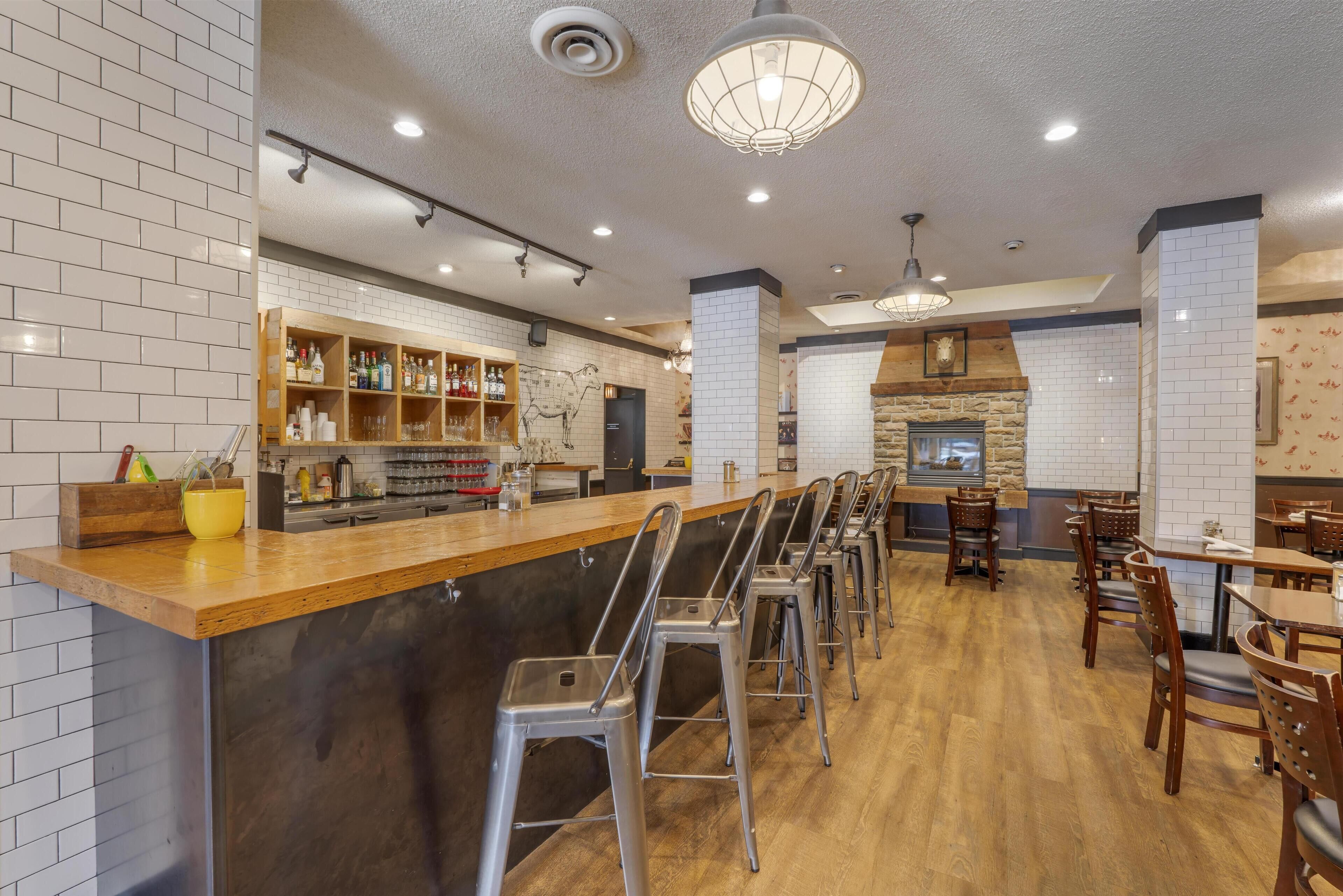 A restaurant with a bar area, high stools, and a stone fireplace.