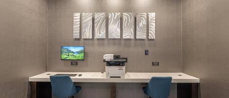 Un espacio de oficina moderno con un escritorio grande, dos sillas azules, una impresora y un monitor en la pared.