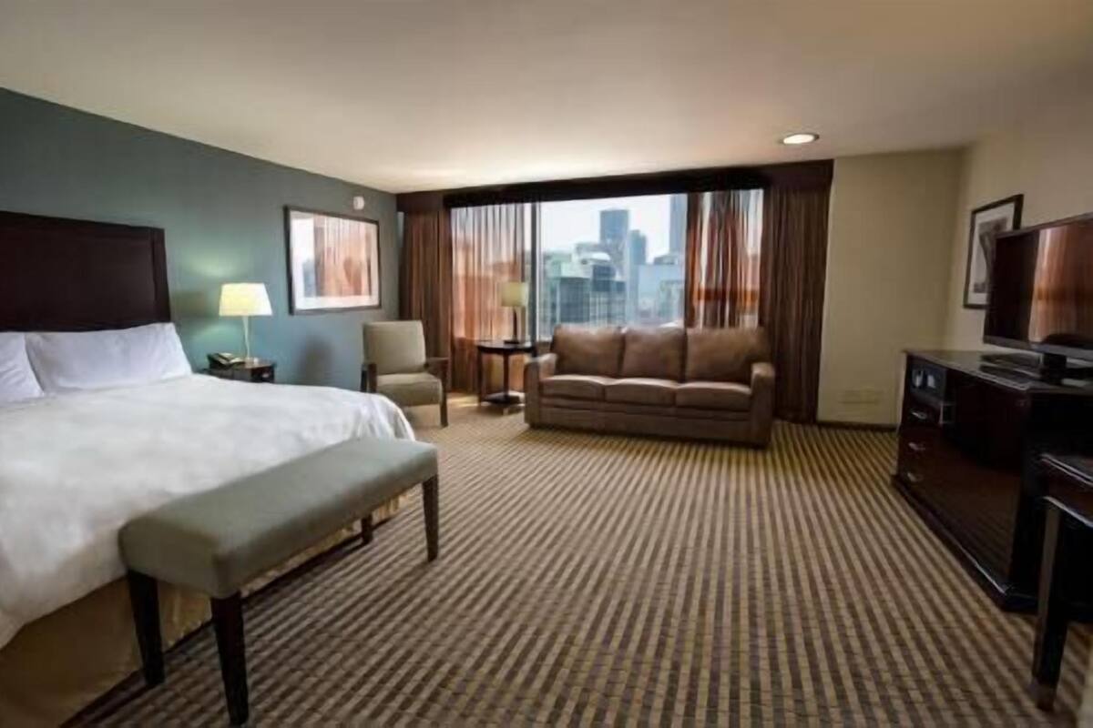 A hotel room with a bed, a sofa, a desk, and a TV.