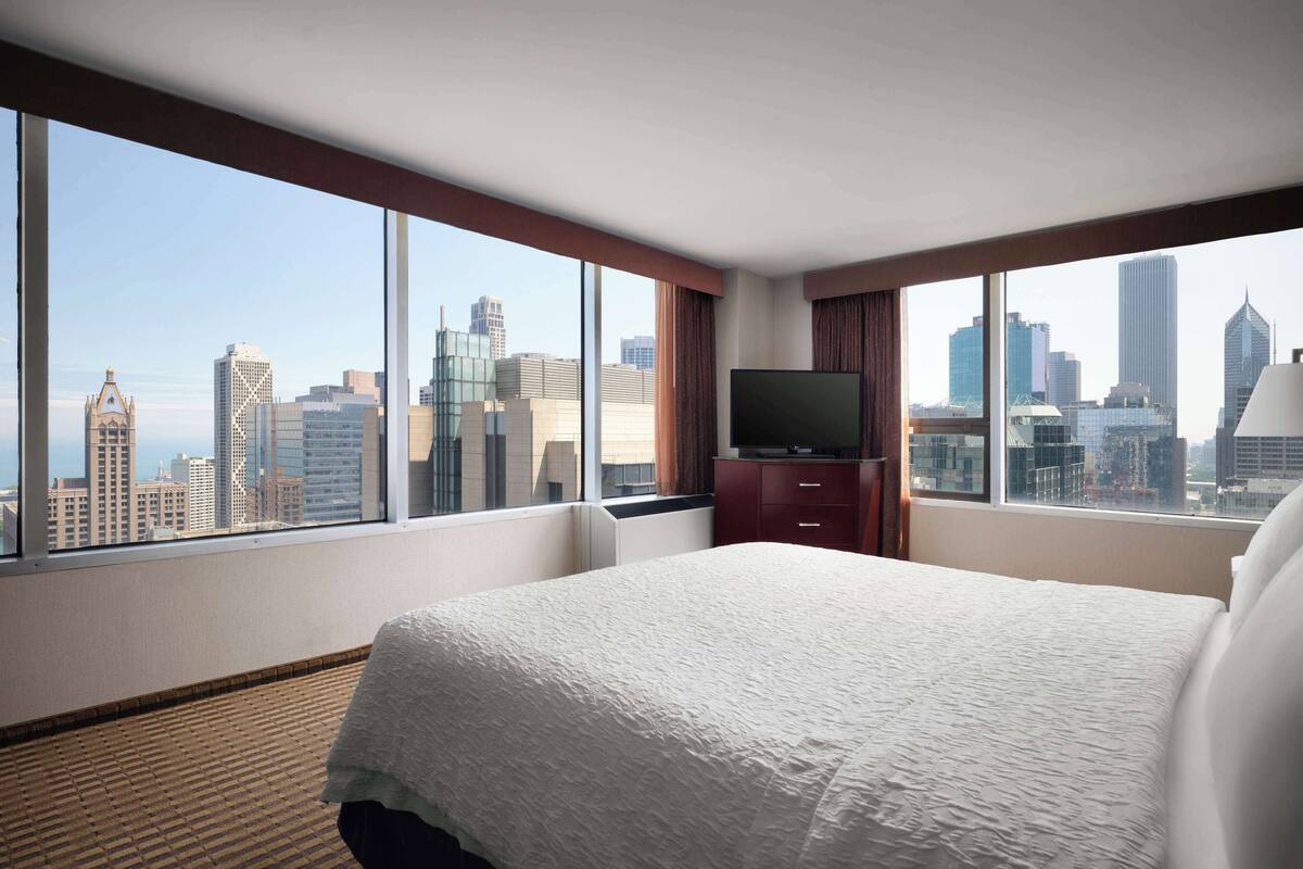 A hotel room with a large bed, a TV, and a city view.