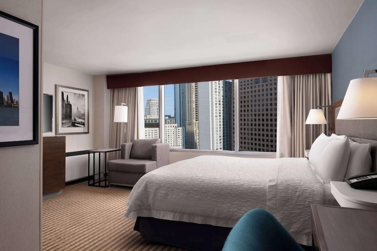Une chambre d’hôtel avec un grand lit, un bureau, une chaise et une vue sur les bâtiments de la ville.