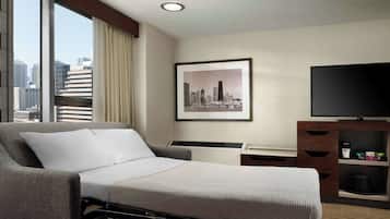 A hotel room with a bed, a TV, a desk, and a window with a cityscape view.
