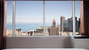 Quarto de hotel com uma janela ampla que oferece vista para a paisagem urbana, incluindo um edifício imponente com torre de relógio.