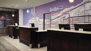 Un espace d’accueil doté de comptoirs de réception en bois foncé, d’une fresque murale violette et de luminaires suspendus.