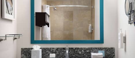 A bathroom with a large mirror, granite countertop, and a shower visible in the mirror.