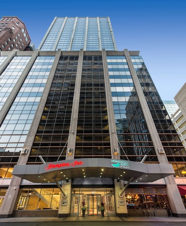 A hotel with a modern glass facade, a prominent Hampton Inn sign, and a Homewood Suites by Hilton sign.