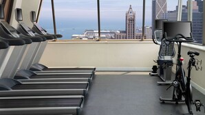 Uma academia com esteiras, bicicleta ergométrica e remo, com vista para a cidade através de grandes janelas.