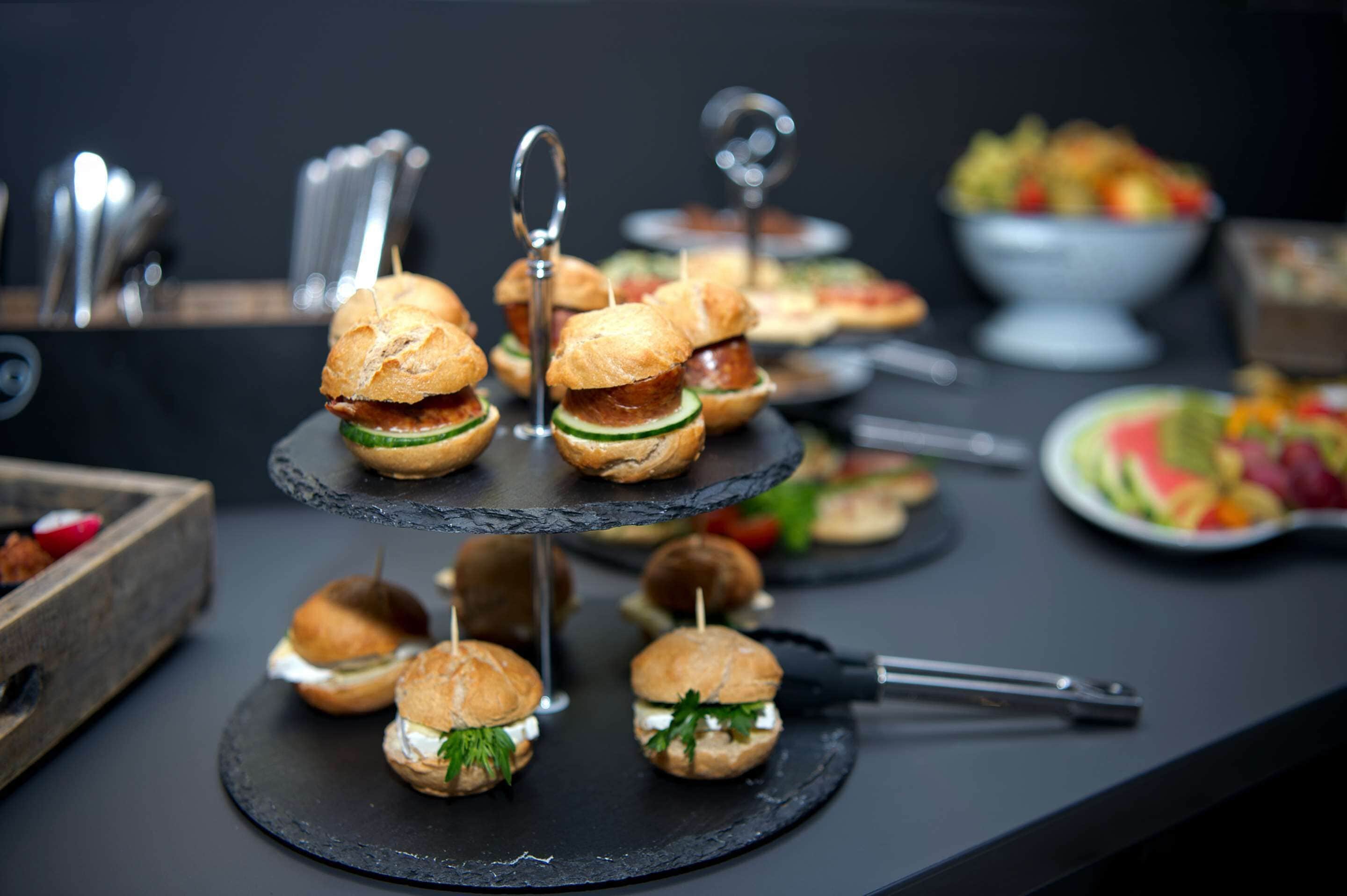 A buffet table with various food items including mini sandwiches, fruit, and a bowl of salad.