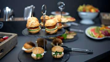 Una mesa de buffet con diversas opciones de comida, incluyendo sándwiches pequeños, fruta y un tazón de ensalada.