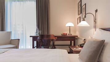 Habitación de hotel con cama, escritorio, silla, lámpara y vistas a la ciudad a través del ventanal.