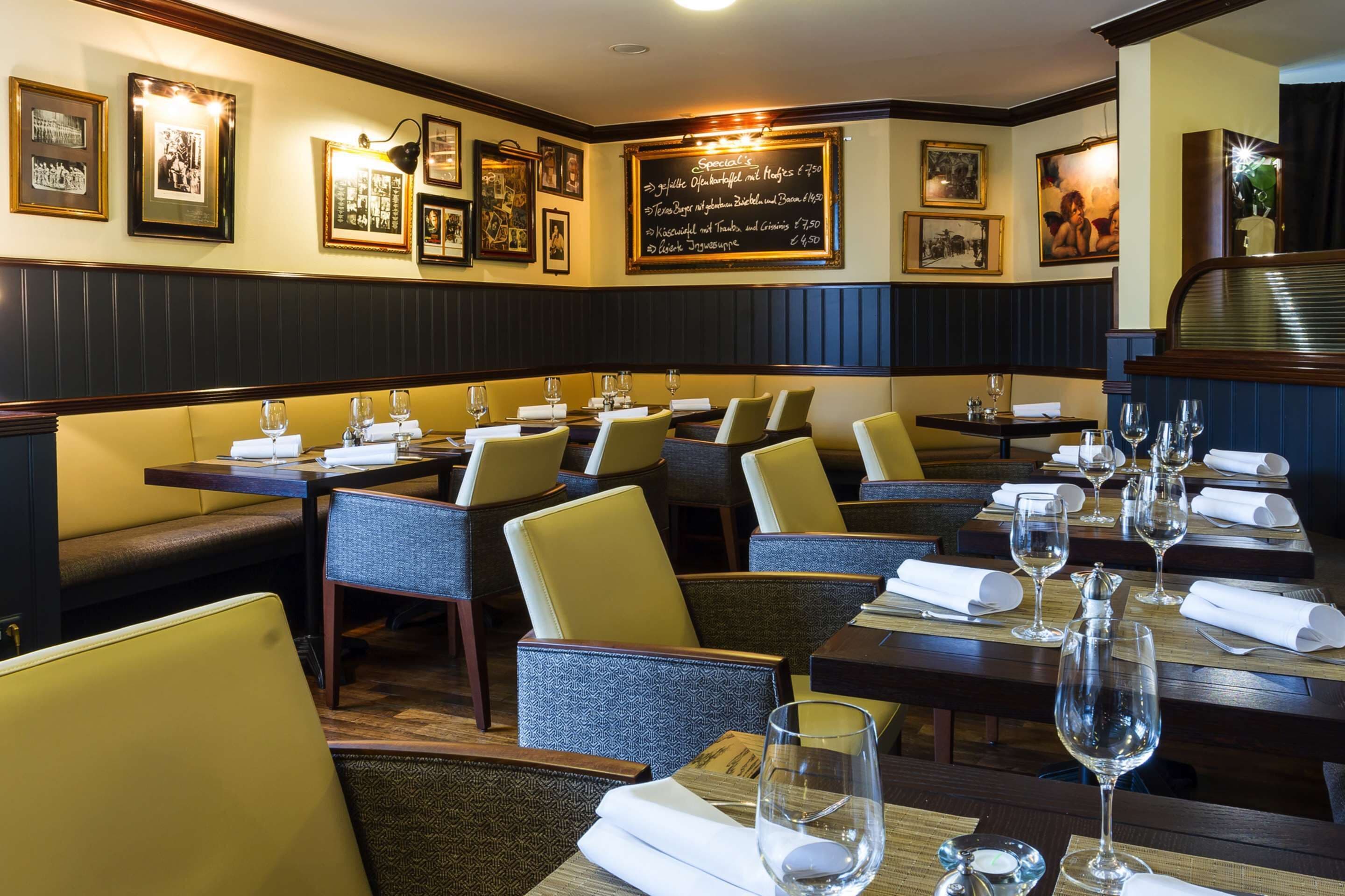 Un restaurant avec des banquettes et des tables, chacune étant agrémentée de verres à vin et de serviettes.