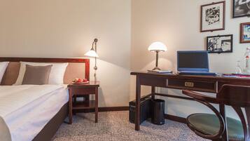 A hotel room with a bed, desk, chair, lamp, laptop, and framed pictures on the wall.