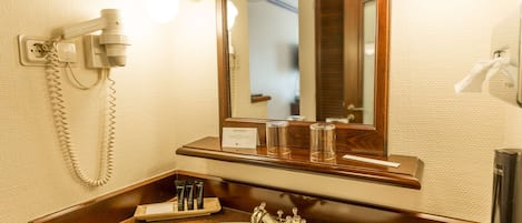 Un baño de hotel con lavamanos, espejo y secador de pelo fijado a la pared.