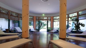 A sunlit room with wooden floors, large windows, and several white lounge chairs. - MAXX Hotel Jena (Jena)