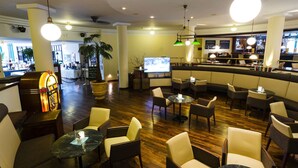 A bar area with a jukebox, seating, and a television screen. - MAXX Hotel Jena (Jena)