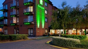A Holiday Inn hotel with a prominent green sign, multiple balconies with lights, and a brick facade.