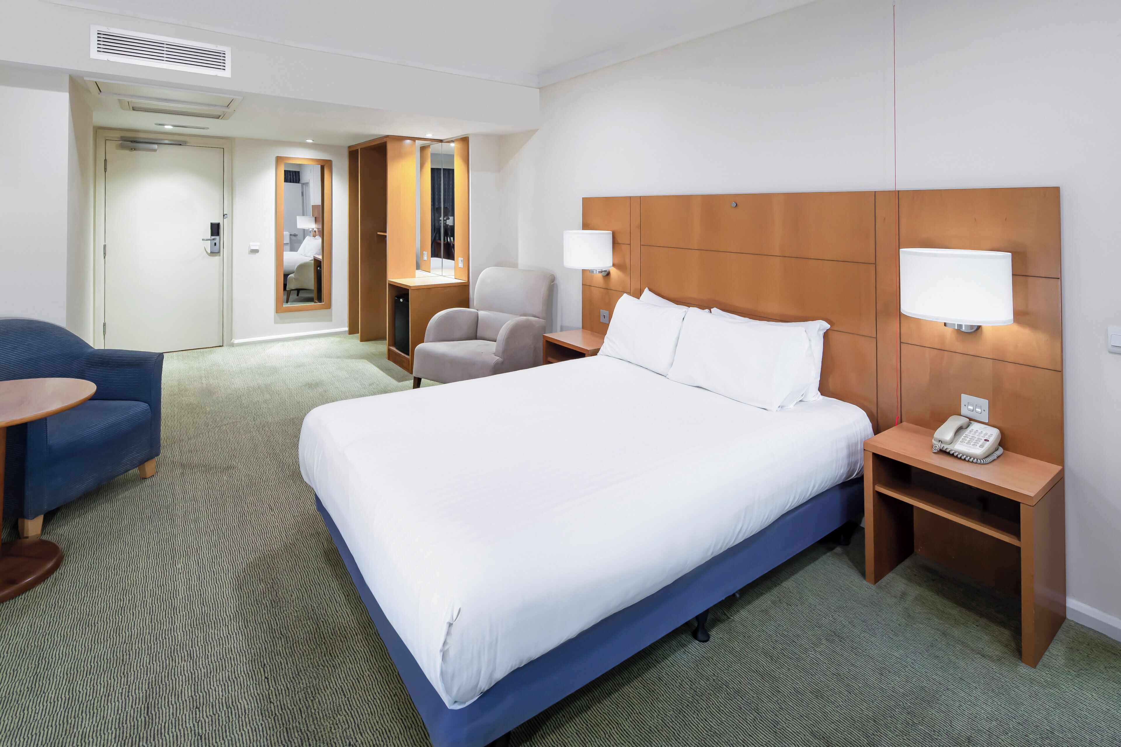 A hotel room with a large bed, a desk, a chair, and a small table.