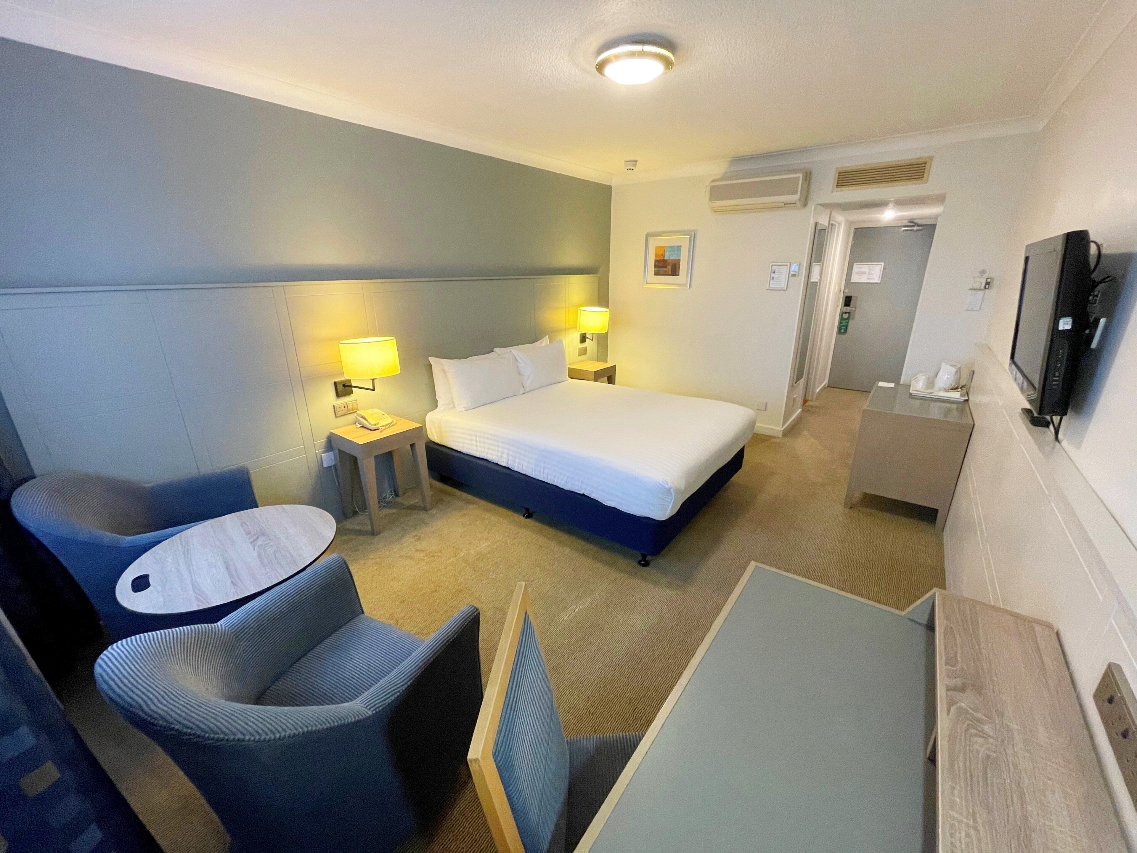 Una habitación de hotel con una cama, una silla, un escritorio, un televisor y una lámpara.