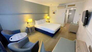 Una habitación de hotel con una cama, una silla, un escritorio, un televisor y una lámpara.