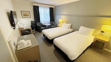 A hotel room with two beds, a desk, a chair, a small table, and a TV.