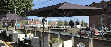 Outdoor seating with umbrellas, a view of the water, and boats in the background.
