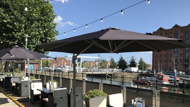 Outdoor seating with umbrellas, a view of the water, and boats in the background.