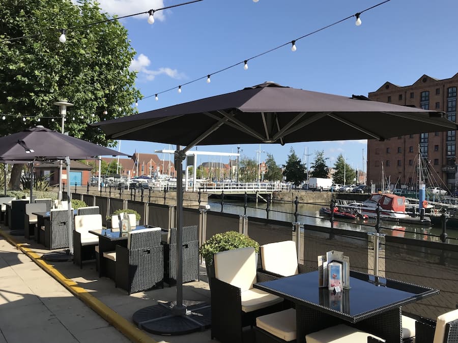 Outdoor seating with umbrellas, a view of the water, and boats in the background.