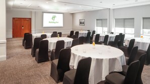 A conference room with multiple round tables, black chairs, and a projector screen displaying the Holiday Inn logo.