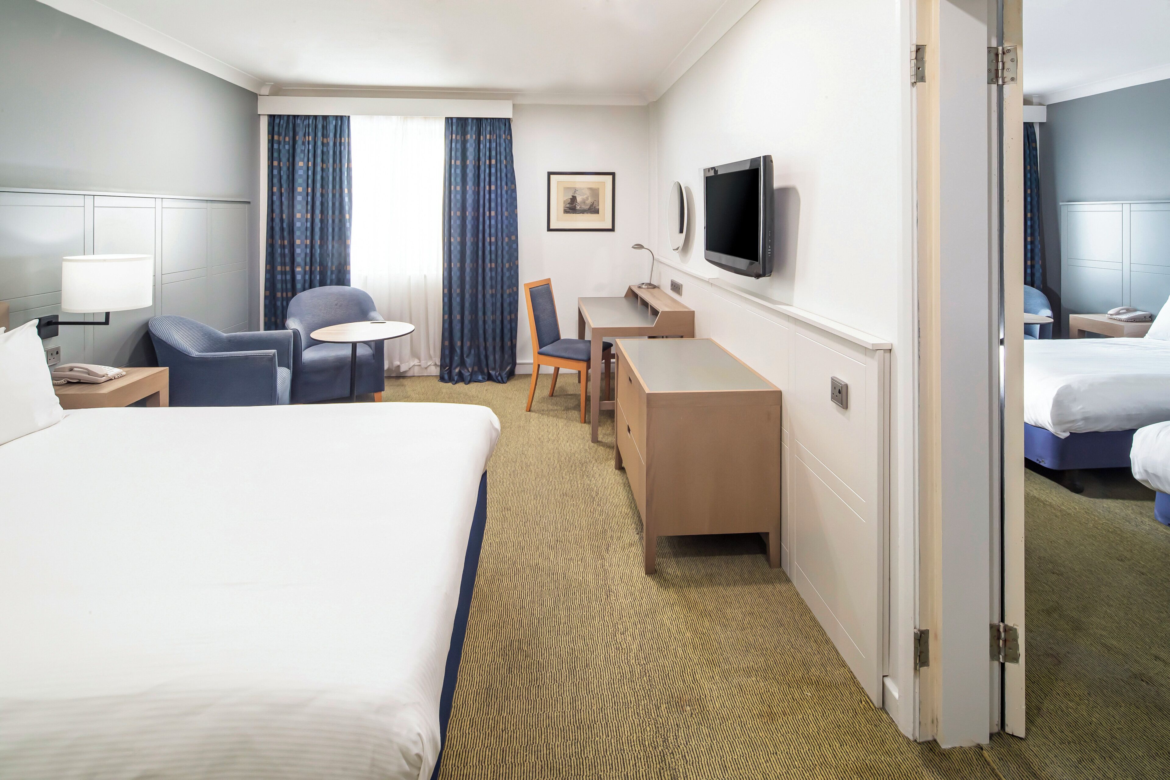 A hotel room with a large bed, a desk, two chairs, a television, and a door.