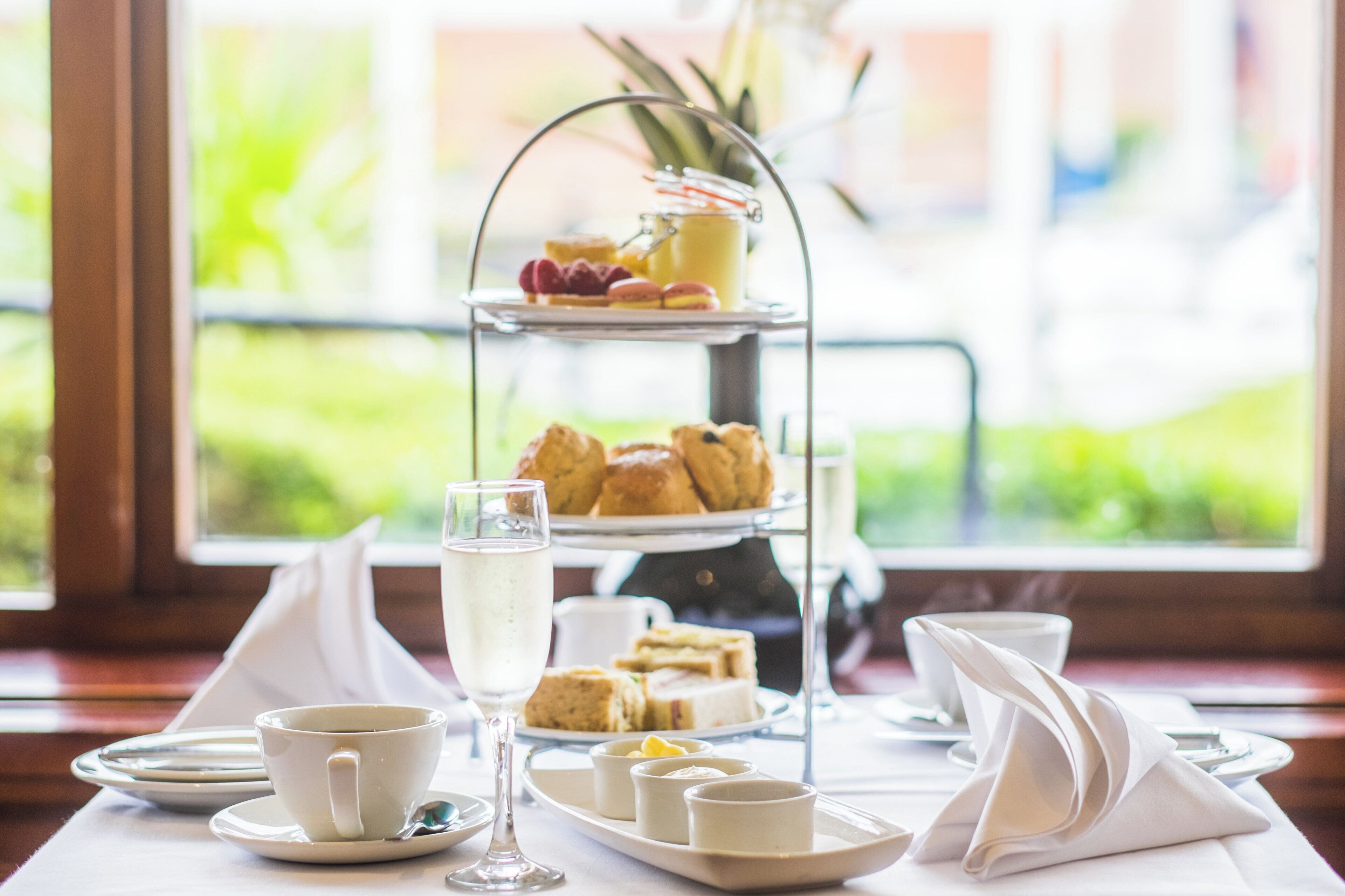 A three-tiered dessert stand with pastries and a glass of juice, a cup of coffee, and a glass of milk on a table with a napkin and cutlery.