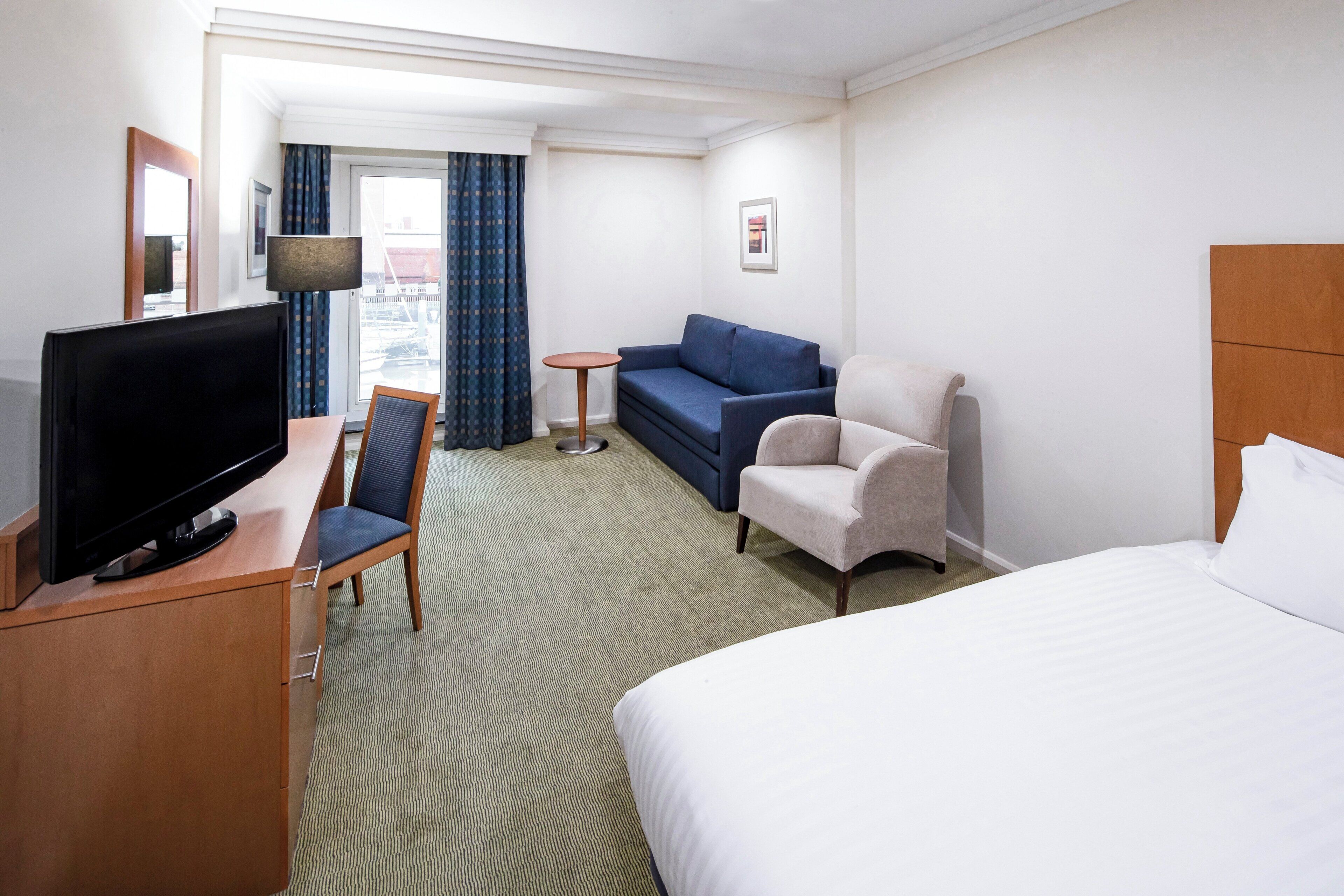 Een hotelkamer met een bed, een bureau met een televisie, een bank, een stoel en een kleine tafel.