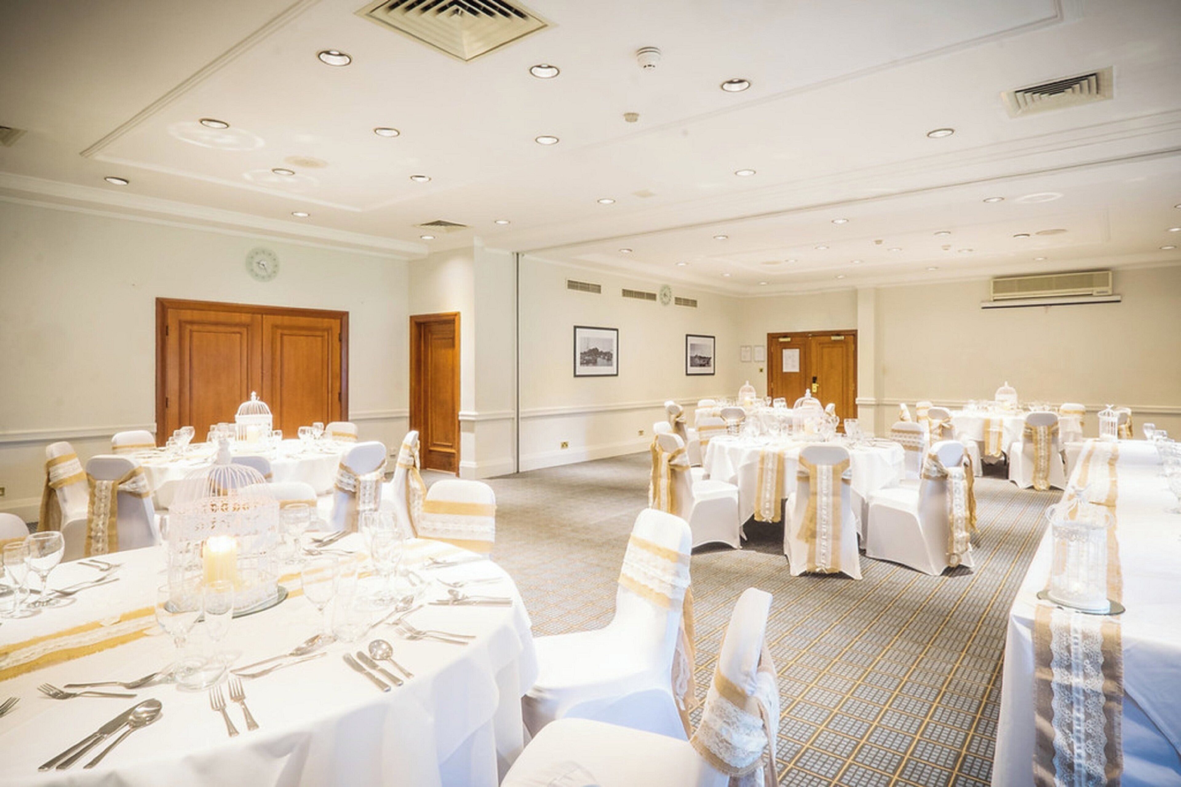A banquet hall with round tables set for dining, equipped with cutlery and glassware.
