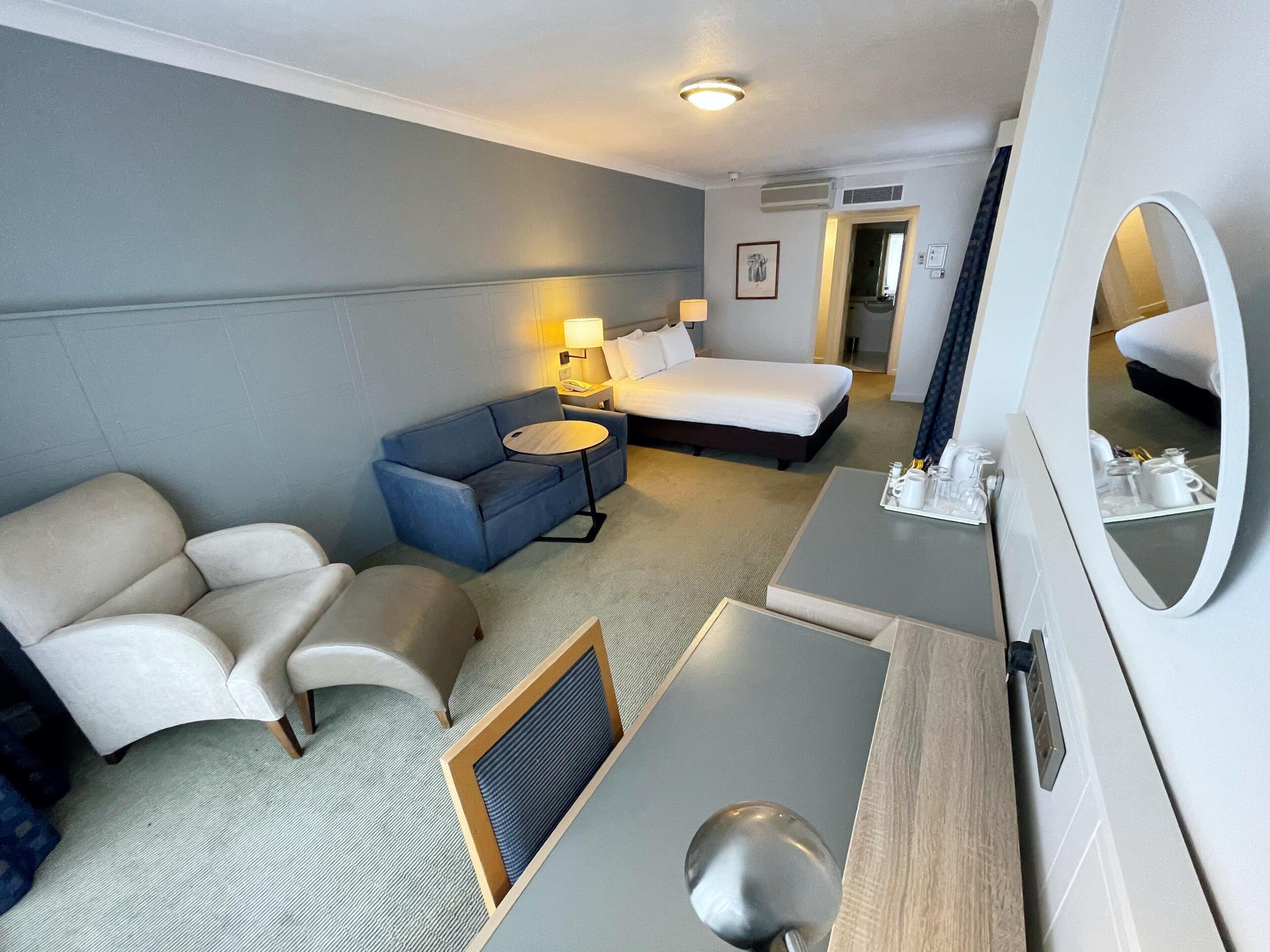 A hotel room with a bed, a sofa, a desk, and a mirror.
