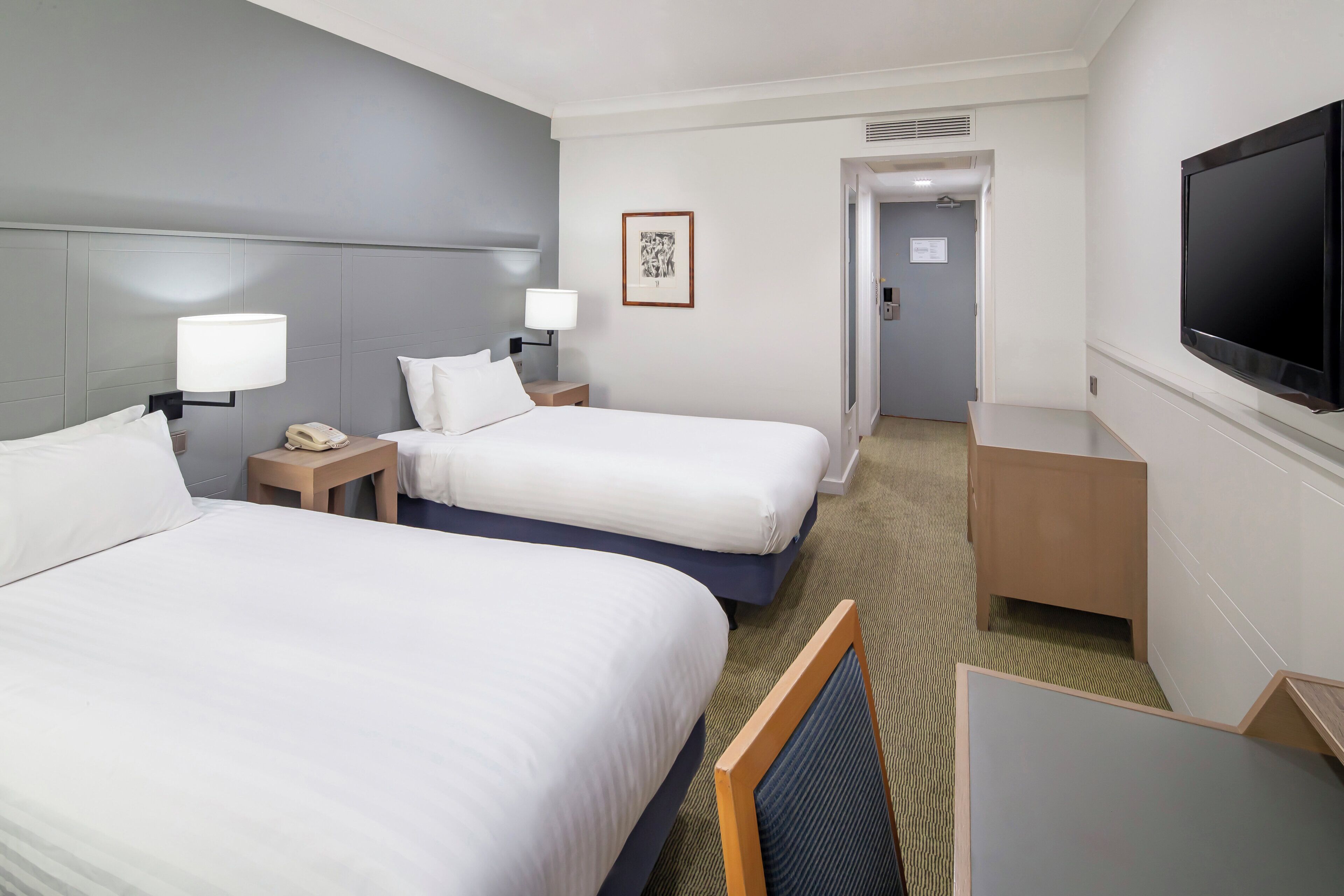 A hotel room with two beds, a TV, a desk, and a bathroom visible through an open door.