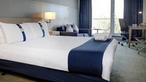 A hotel room with a large bed, a desk, a chair, a lamp, and a view of the outdoors.