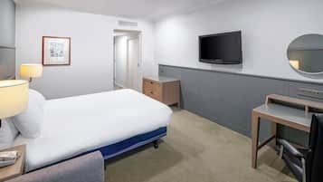 Una habitación de hotel con cama, mesita de noche, lámpara, escritorio, silla, televisor y espejo.