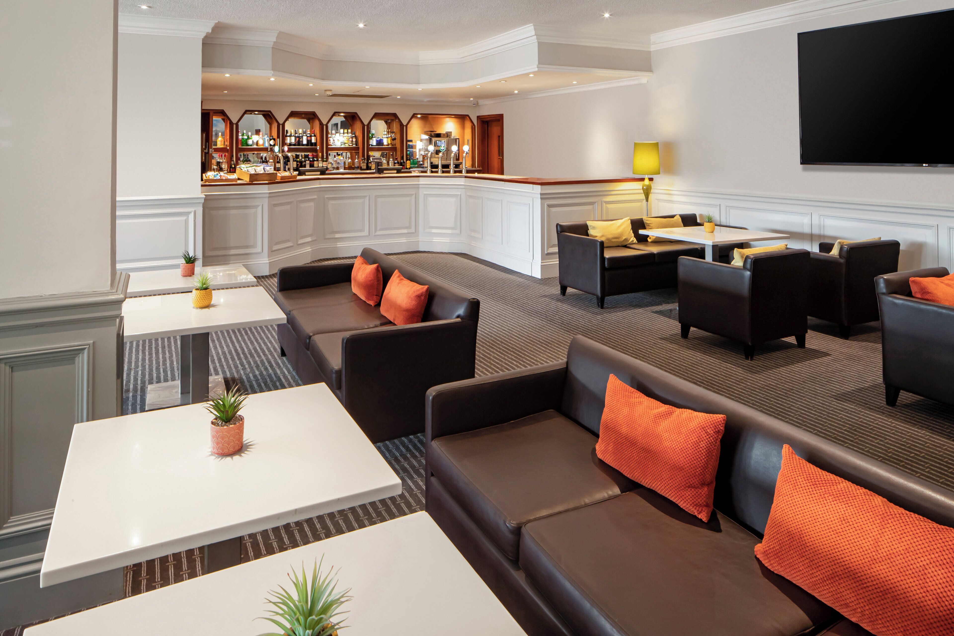 A hotel lobby with a bar area, seating arrangements, and a flat-screen TV mounted on the wall.